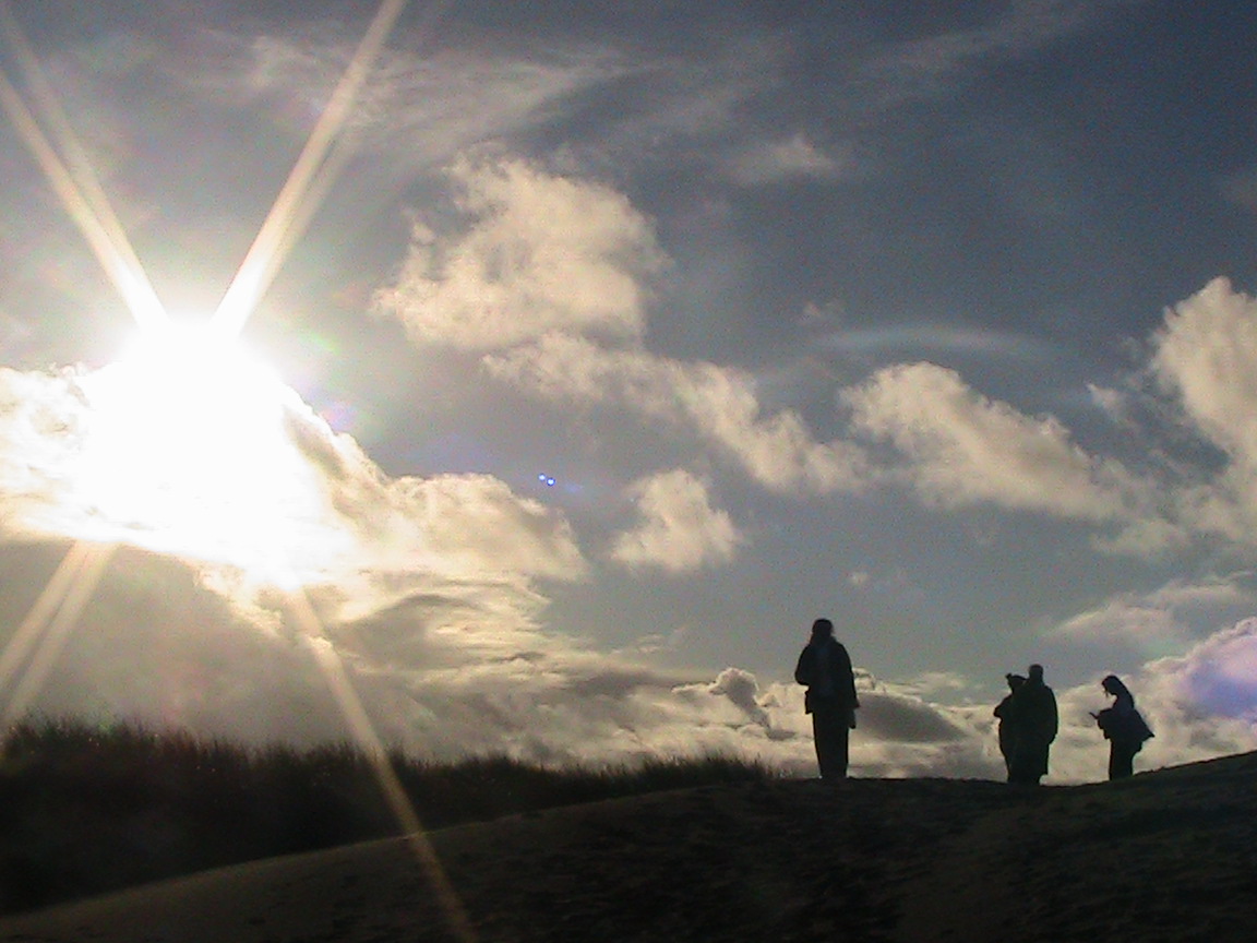 my friends' silhouettes on top of a sand dune with  the sun beaming in the background